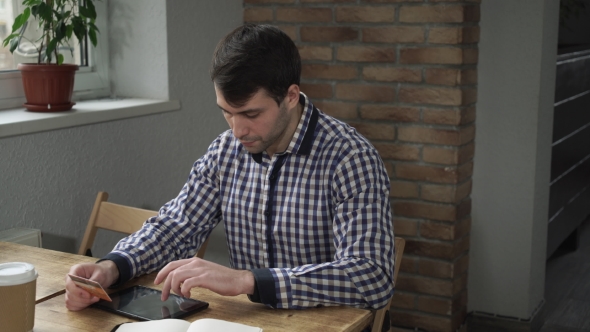 Man With Tablet And Credit Card Sitting In a Cafe And Pay For The Purchase.