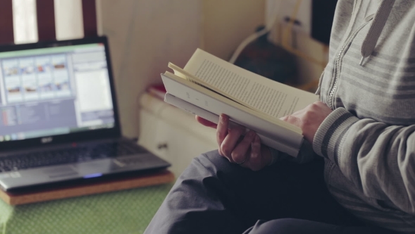 Woman Reading a Book At Home Near Laptop.