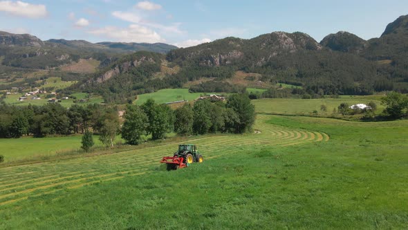 A tractor harvesting grass across farmland and fields in the beautiful nature of Norway alt