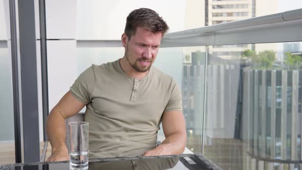 A Young Handsome Man Acts Upset As He Sits on a Balcony in a Luxurious Apartment alt