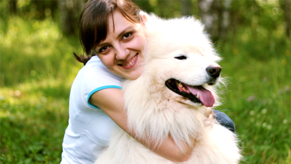 Young Woman Hugging her Big White Dog on Bright Park Background