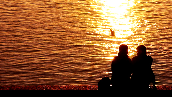 Silhouettes of Two Young Couple Enjoying the Sunset on the Sea Coast