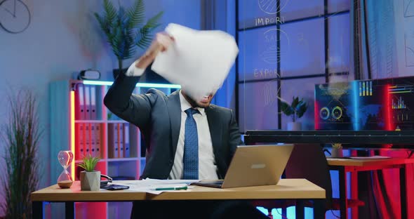 Businessman in Suit Getting Good News on Laptop Screen in Evening Office and Scattering Papers alt