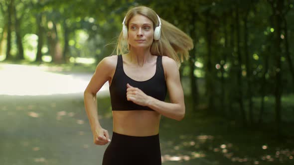 Follow Shot Portrait of Positive Carefree Active Middle Aged Woman Wearing Headset Running in Public alt