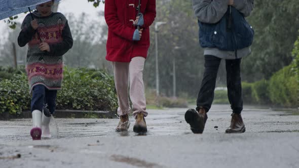 Three kids running happy in the rain and puddles with umbrellas alt