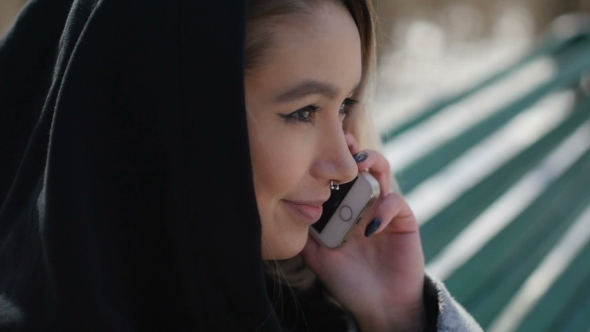 Young Girl Talking On The Phone While Sitting On a Bench In The Park