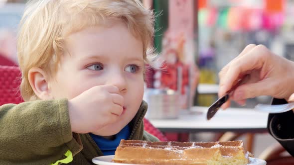 Little Boy Eating A Waffle In A Street Cafe