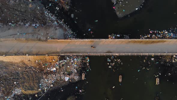 Aerial top down of old narrowed suspension bridge with scooter driving over a polluted river filled alt