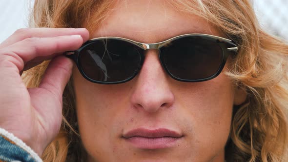 Close up portrait. Stylish hipster man face with long blond hair put on sunglasses