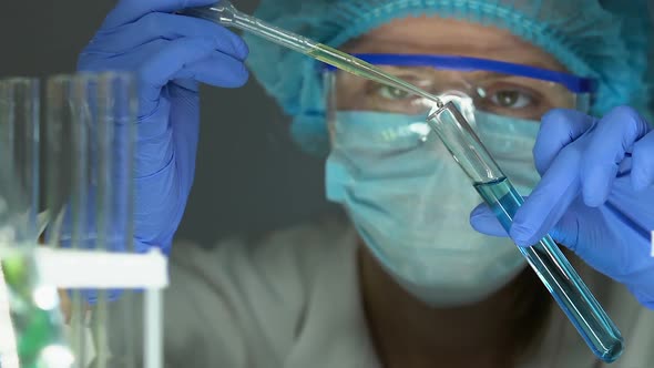 Female Chemist Dripping Yellow Liquid in Tube With Blue Substance, Experiment alt