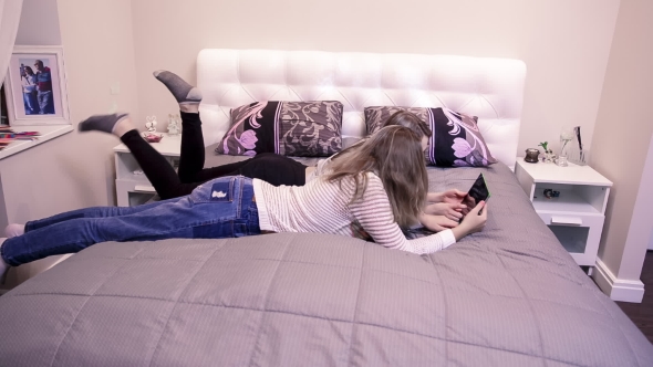 Two Girls Lying In Bed And Looking At The Tablet