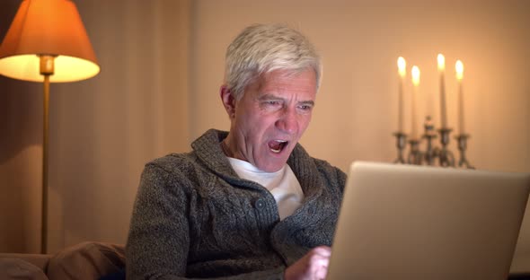 Portrait of Tired Senior Man Working in Home Office on Laptop and Yawning alt