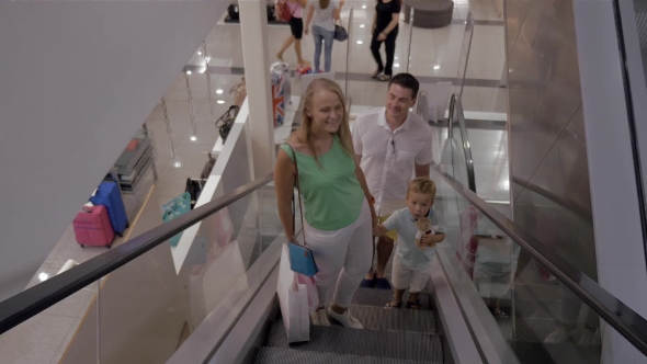 Young Family With Child Riding Escalator In Shopping Center alt