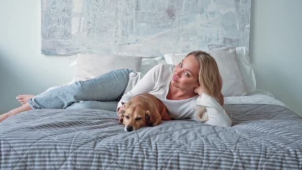 Young Beautiful Caucasian Blonde Woman in Home Clothes on the Bed with Her Cute Little Brown alt