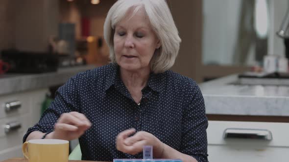 Senior Adult woman taking medicine at home in kitchen