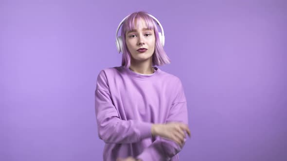 Pretty Girl with Dyed Violet Hair Dancing with Wireless Headphones on Purple Studio Background alt