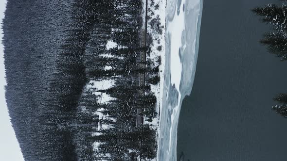Vertical video: frozen winter river in Romania highlands with snow covered mountain in the backgroun alt