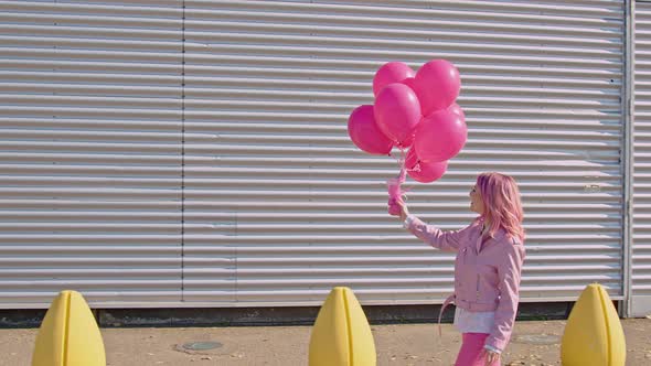 Happy woman with pink hair holding pink balloons walking in the street alt