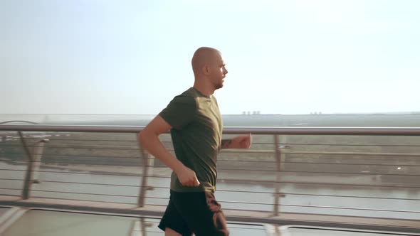 Young Man in Sports Uniform Runs on the Pedestrian Bridge at Dawn alt
