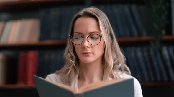 Closeup Blonde Woman in Vintage Eyeglasses Reading Interesting Paper Book Turning Page at Library alt