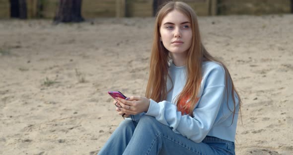 Young Girl Sitting on the Beach and Holding a Telephone in her Hands