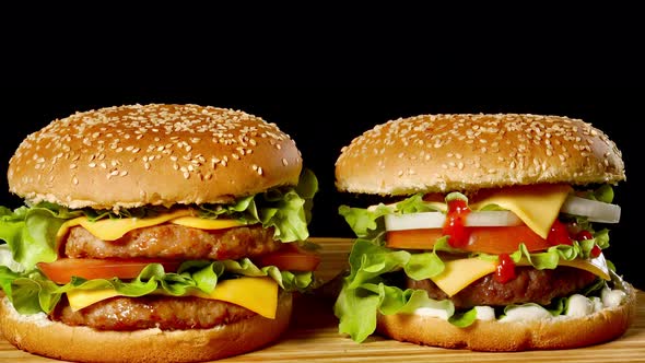 Close-up of Two Appetizing Burgers with Sesame Buns Rotating on Black Background, of Fast Food alt