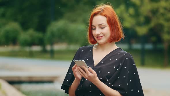 Pretty Caucasian Lady Girl Stand Outdoors in City Park Look at Mobile Phone Use Urban Wifi Beautiful alt