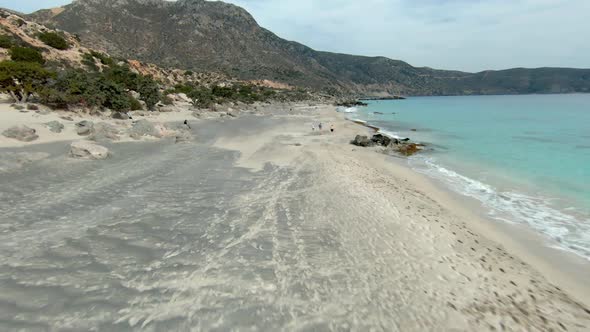 Three friends and a dog running by the ocean. Kedrodasos beach, Greece, Europe. FPV drone view. alt