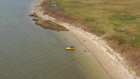 An aerial shot over a salt marsh on a sunny day. In the shot is a man heading out in a yellow kayak alt
