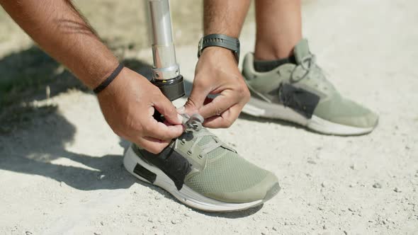 Closeup of Man with Bionic Leg Tying Laces on Athletic Shoes alt