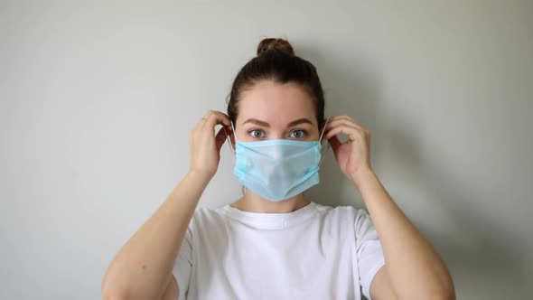 Woman Is Putting on Mask on Face in Coronavirus Pandemic on Grey Background.