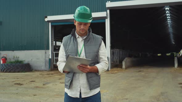 Focused Engineer Making Notes at Modern Cowshed Building in Protective Helmet alt
