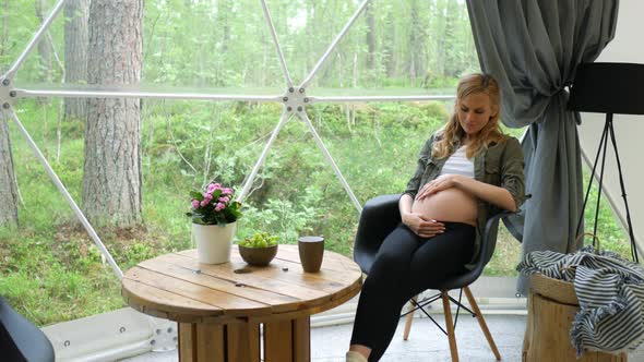 pregnant woman stroking her belly by the window of a dome tent in the forest