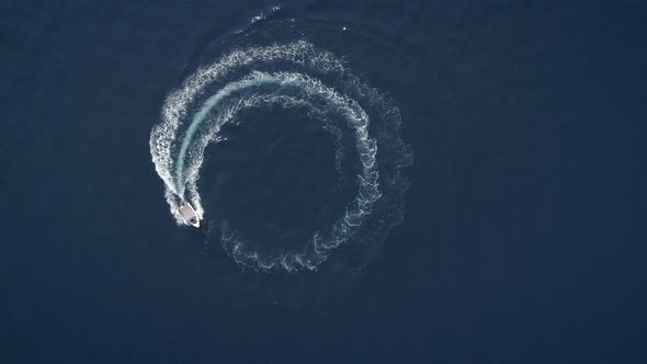 Aerial view of a boat driving in circles forming waves around in Greece.