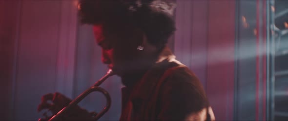 A trumpeter intensely playing in a room with smoke and red neon light alt