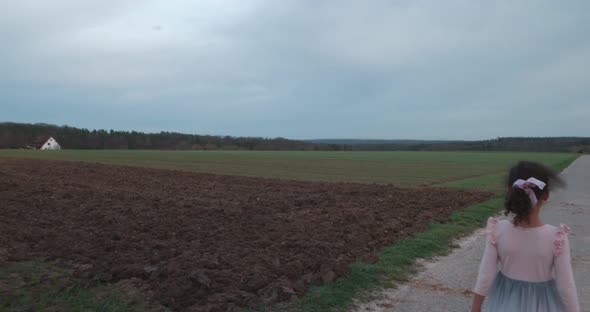 Little girl playing alone on empty countryside road at sunset with house across field in Schonaich G alt