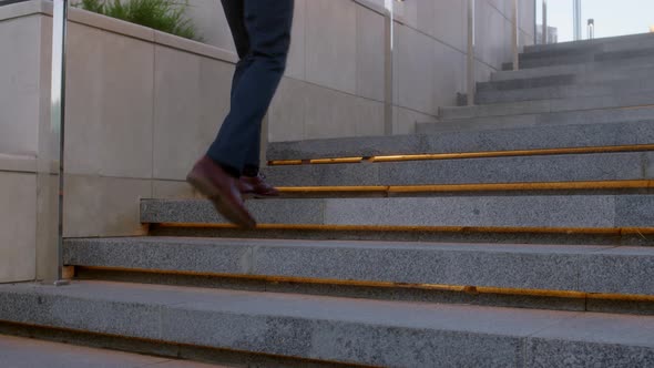 Unrecognizable Young Businessman Climbs Up Backlit Stone Stairs in City alt