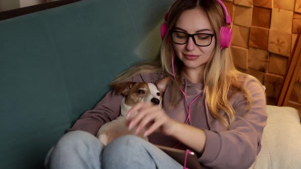 A Girl on the Couch Lies with a Dog in Her Laptop and Listens to Music Through Headphones alt