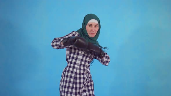 Young Muslim Woman in Boxing Gloves on a Blue Background Looks at the Camera alt