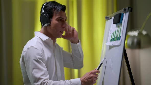 Young Focused Analyst in Headphones Discussing Startup Idea Looking at Graphs on Whiteboard alt