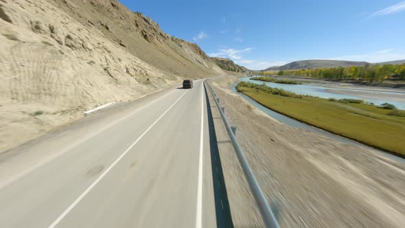 FPV Sports Drone Shot Follow to Black SUV Automobile Riding on Asphalt Road at Mountain River alt