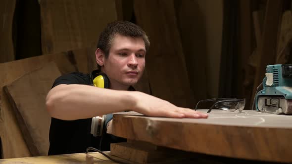 A carpenter blows off wood dust from a workpiece in a workshop alt