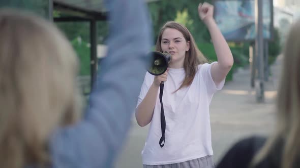 Portrait of Protest Leader with Megaphone Encouraging Crowd with Banners. Young Caucasian Woman alt
