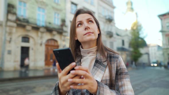 Woman Walking Down an Old Street and Using Smartphone, Taking Photos of Buildings Around alt