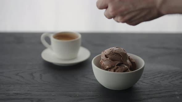 Man Put Chocolate Pieces on Ice Cream Into White Bowl Next to Cup of Espresso alt