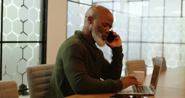 Businessman talking on mobile phone while using laptop 4k alt