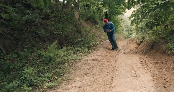 Hiker in Bandana and Phone in Hand Walks Steep Slope in Middle of Summer Forest