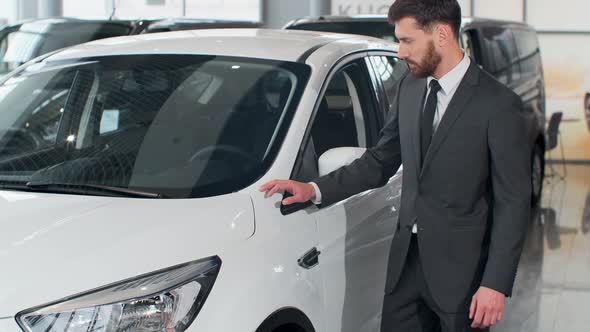 Stylish Man Is Choosing New Automobile Walking Around Luxury Car and Touching It in Car Dealership alt