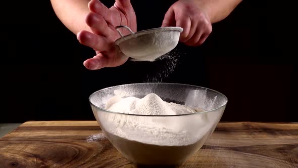 Sifting flour through a sieve into a glass bowl in the kitchen alt