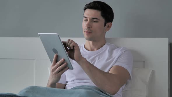 Young Man Browsing Internet on Tablet in Bed alt